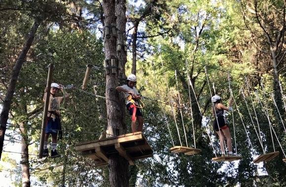 Des jeunes avec casque et harnais sur les parcours suspendus dans les arbres à Riccione Avventura